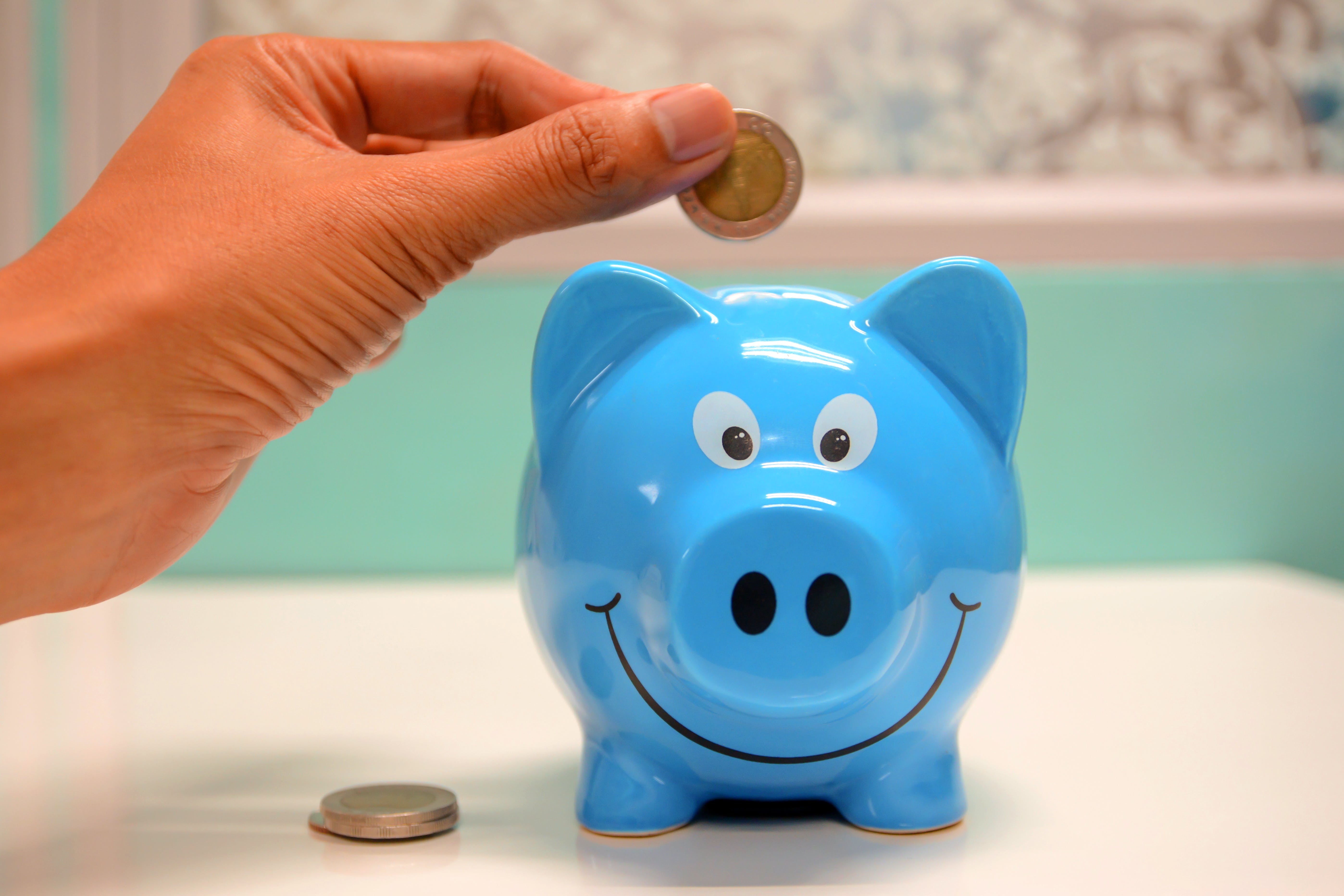 A hand depositing a coin into a piggy bank
